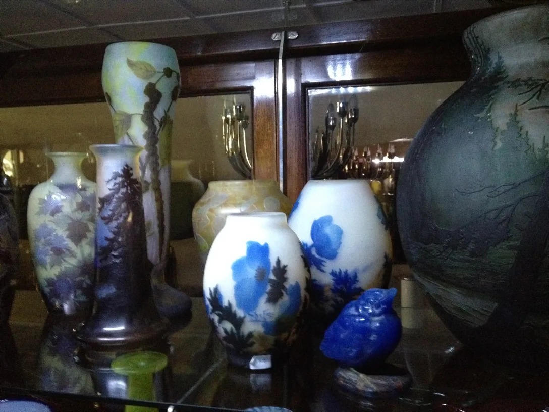 Collection of antiques featuring signed glass Gallé. Decorative vases and figurines on a shelf.