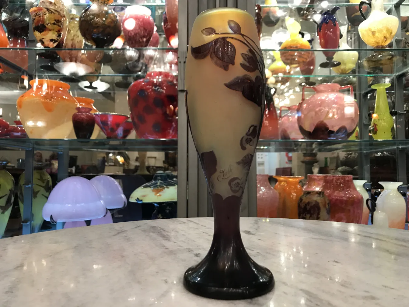 Signed Gallé glass with floral design on light background, surrounded by various antiques.