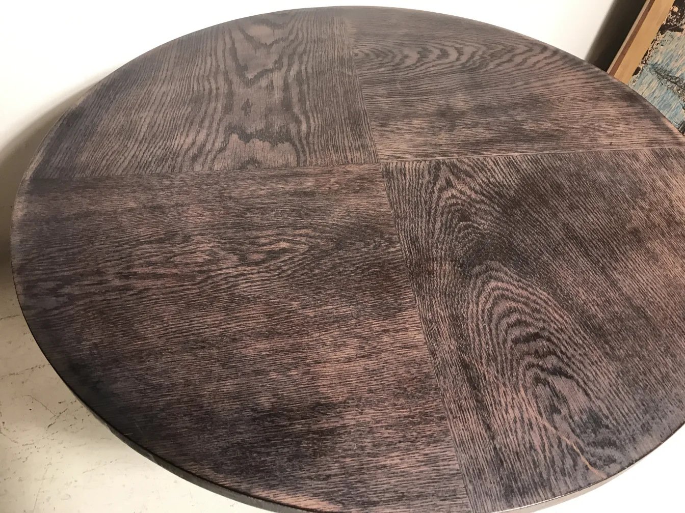 Top view of a small antique round table in a dark color, showing wood grain patterns. Simple background.