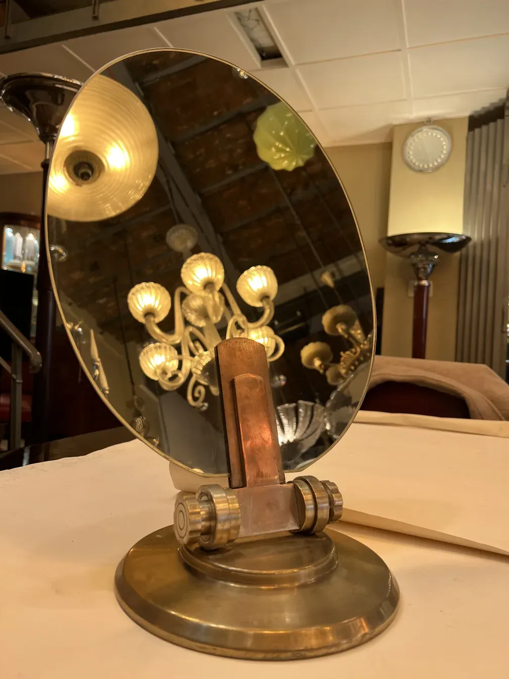 Antique mirror in Art Nouveau style with a cylindrical base, reflecting a modern lamp.