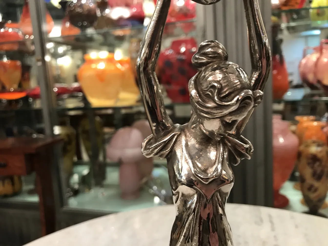 Antique WMF centerpiece shaped like a woman holding a sphere, surrounded by colorful decorative items.
