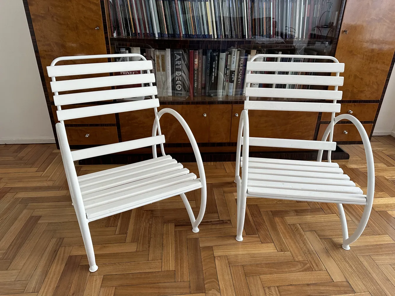 Two antique garden armchairs in white color in an interior setting with wooden floor.