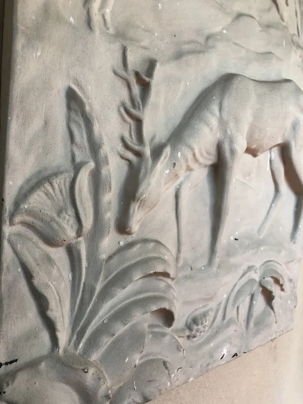 Placa de parede antiga com relevo de flores e folhas em um fundo claro.