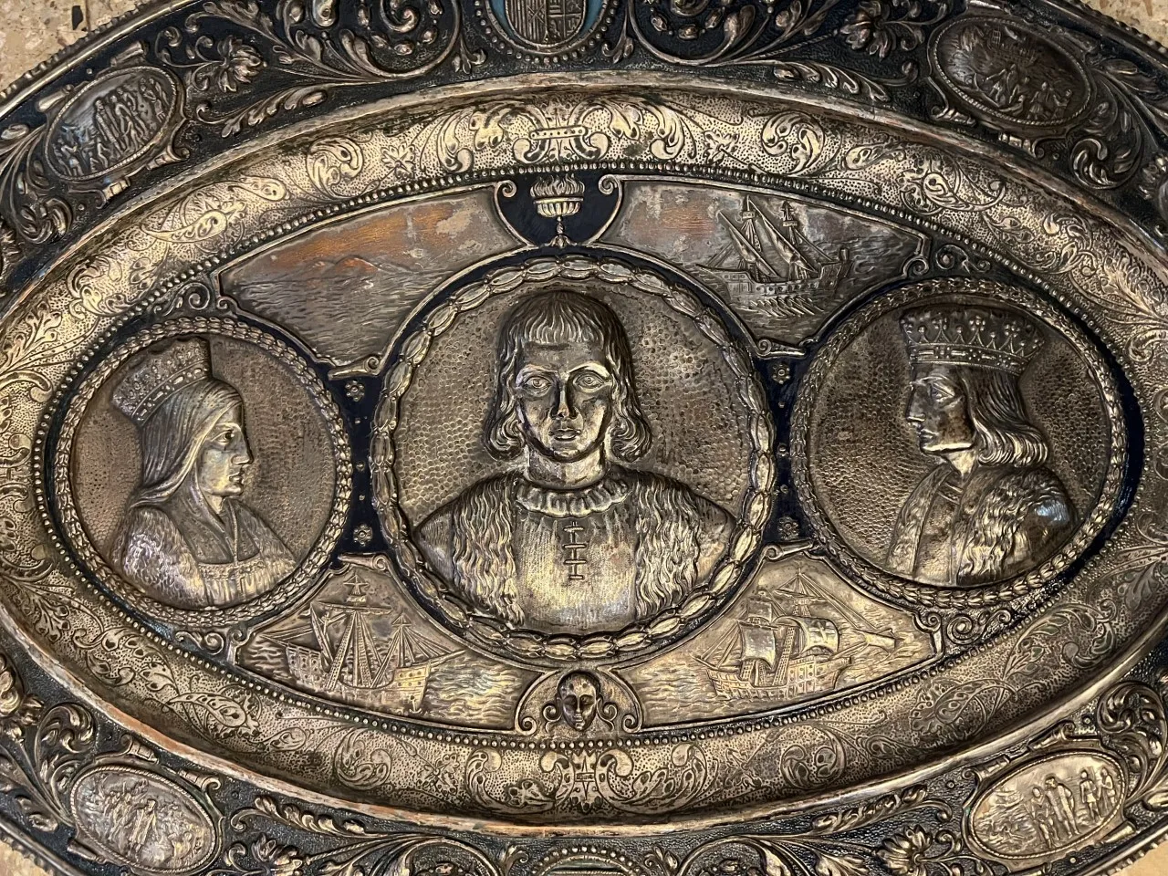 Antique wall plate featuring portraits of people and ships in its design, with a decorative background.