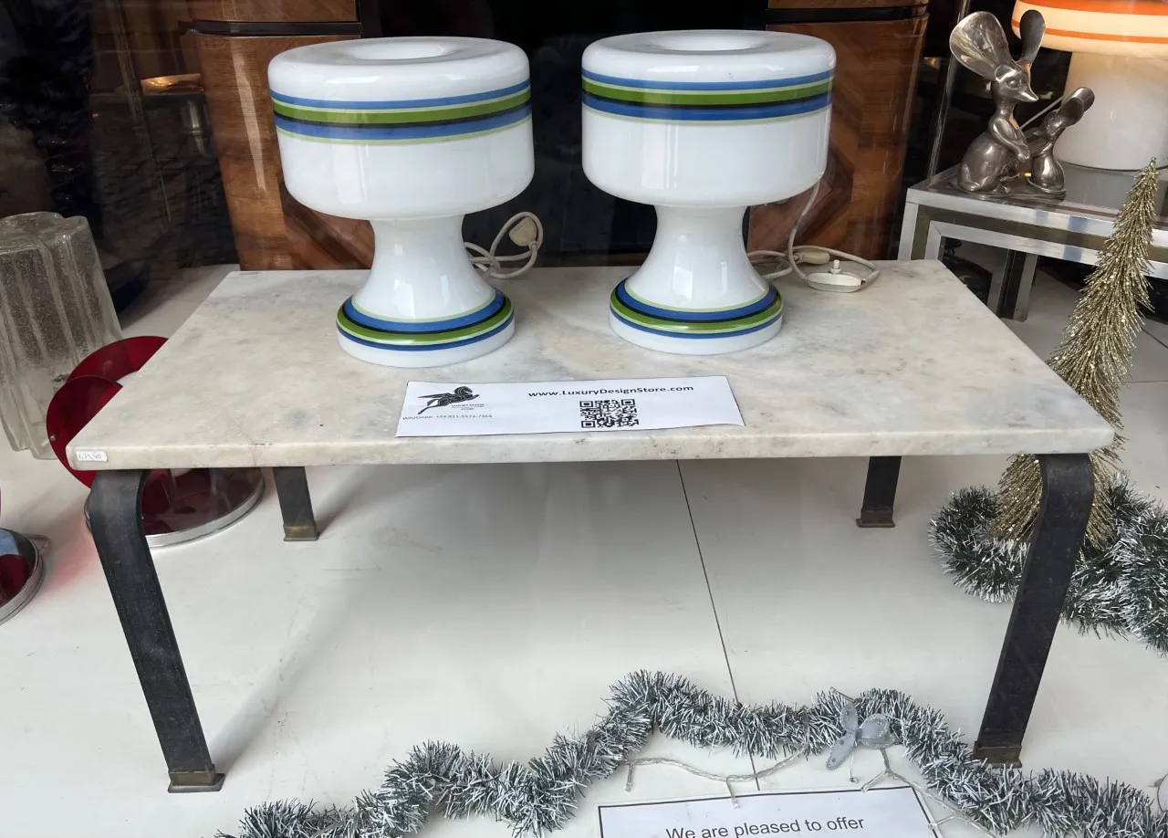 Duas lâmpadas de mesa antigas com bases brancas e listras coloridas estão sobre uma mesa de mármore.