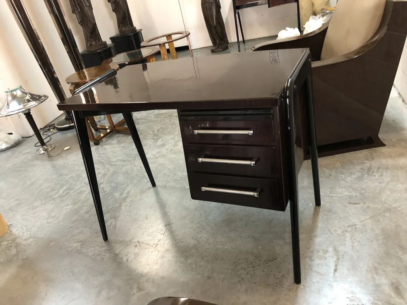 antique desk with long legs and three drawers in a neutral setting