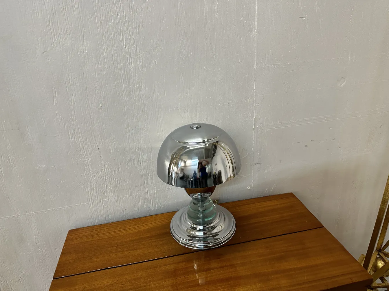Antique table lamp with a shiny finish, round shape, placed on a wooden table.