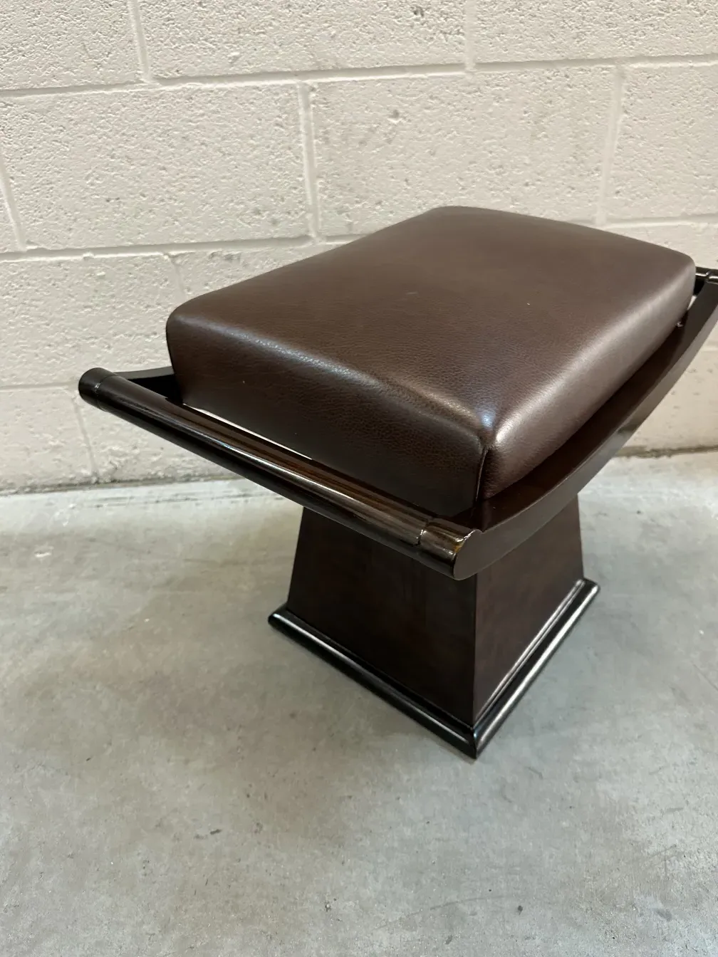 Antique stool with dark seat in neutral setting.