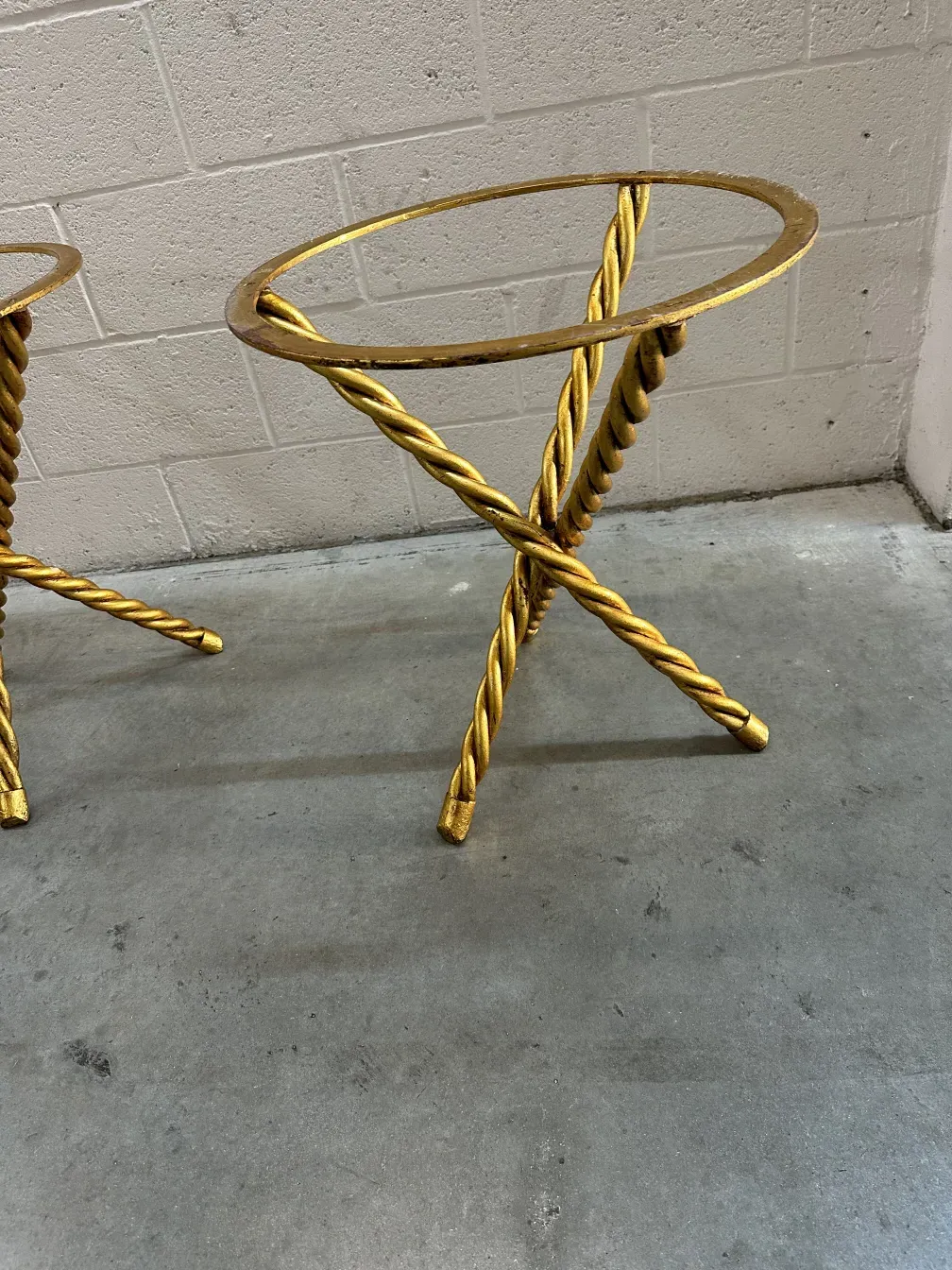 Two antique small tables with gold base and intricate design, set in a concrete environment.