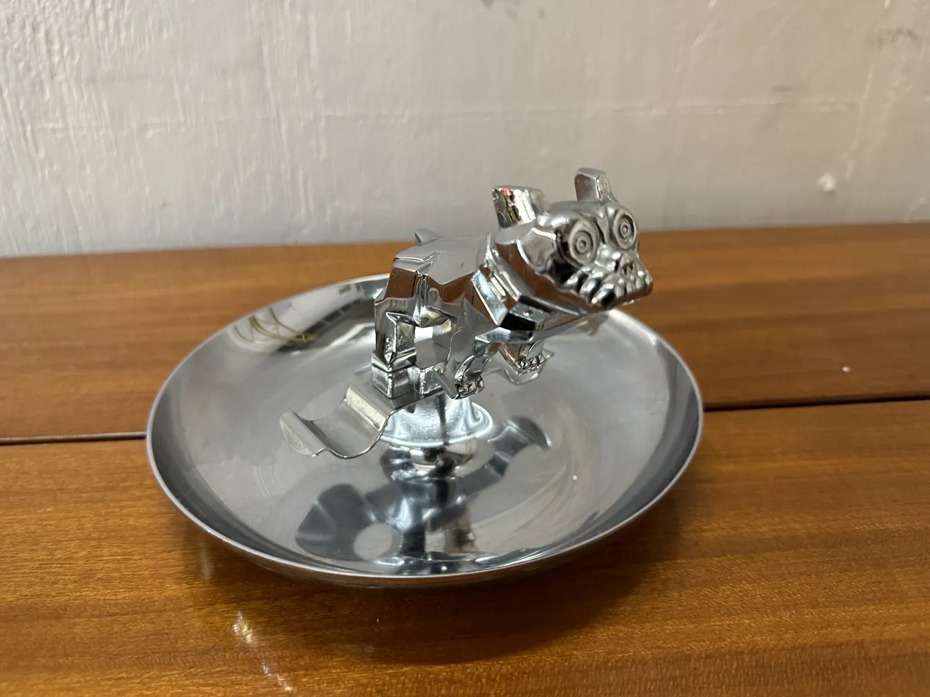 Antique ashtray with a decorative dog, metallic, in a rustic setting.