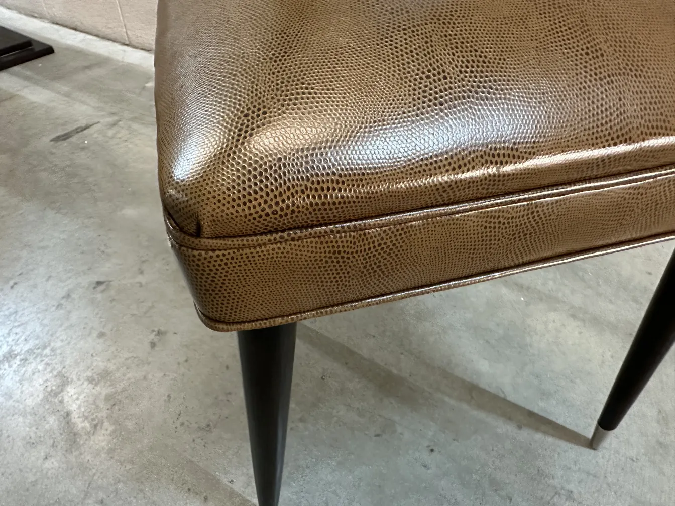 Close-up of an antique chair with dark legs and an elegant design, minimalist surroundings.