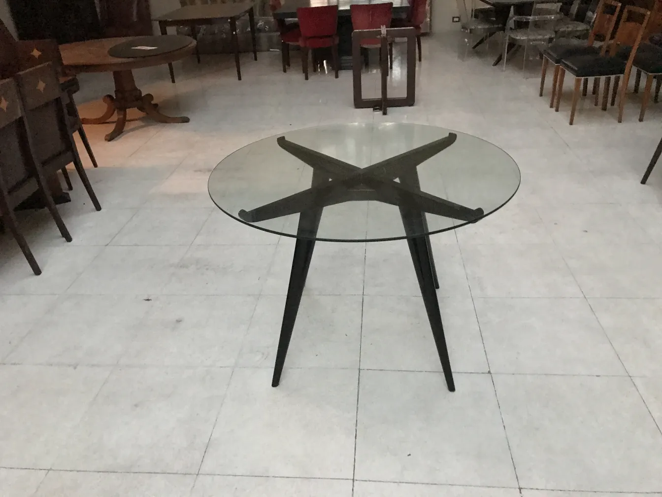 Antique dining table for 4 people with a black base and round glass top, surrounded by chairs in a cozy setting.