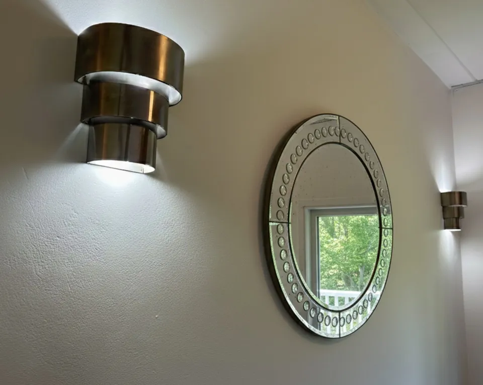 antique pair of sconces with lights on a white wall, with a round mirror nearby