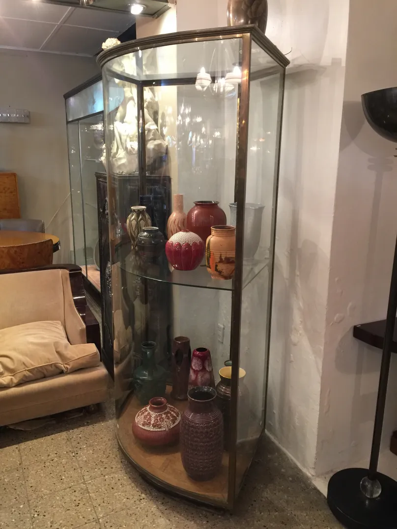 Two antique display cabinets with curved shapes and elegant decorations, showcasing ceramics in various colors.