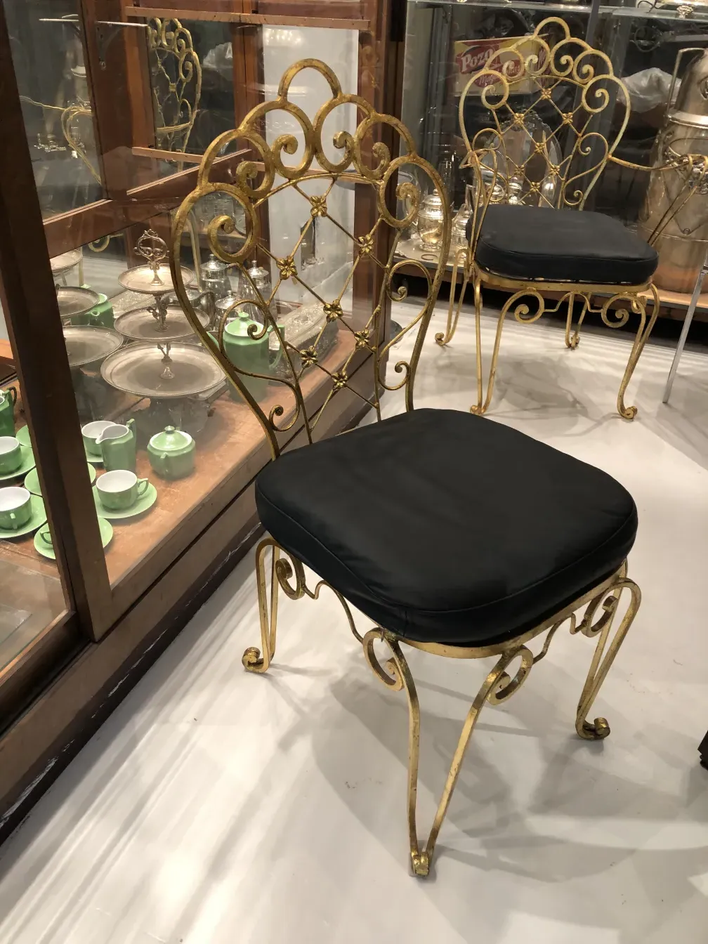 Two antique garden chairs with golden frames and dark seats in a vintage setting.