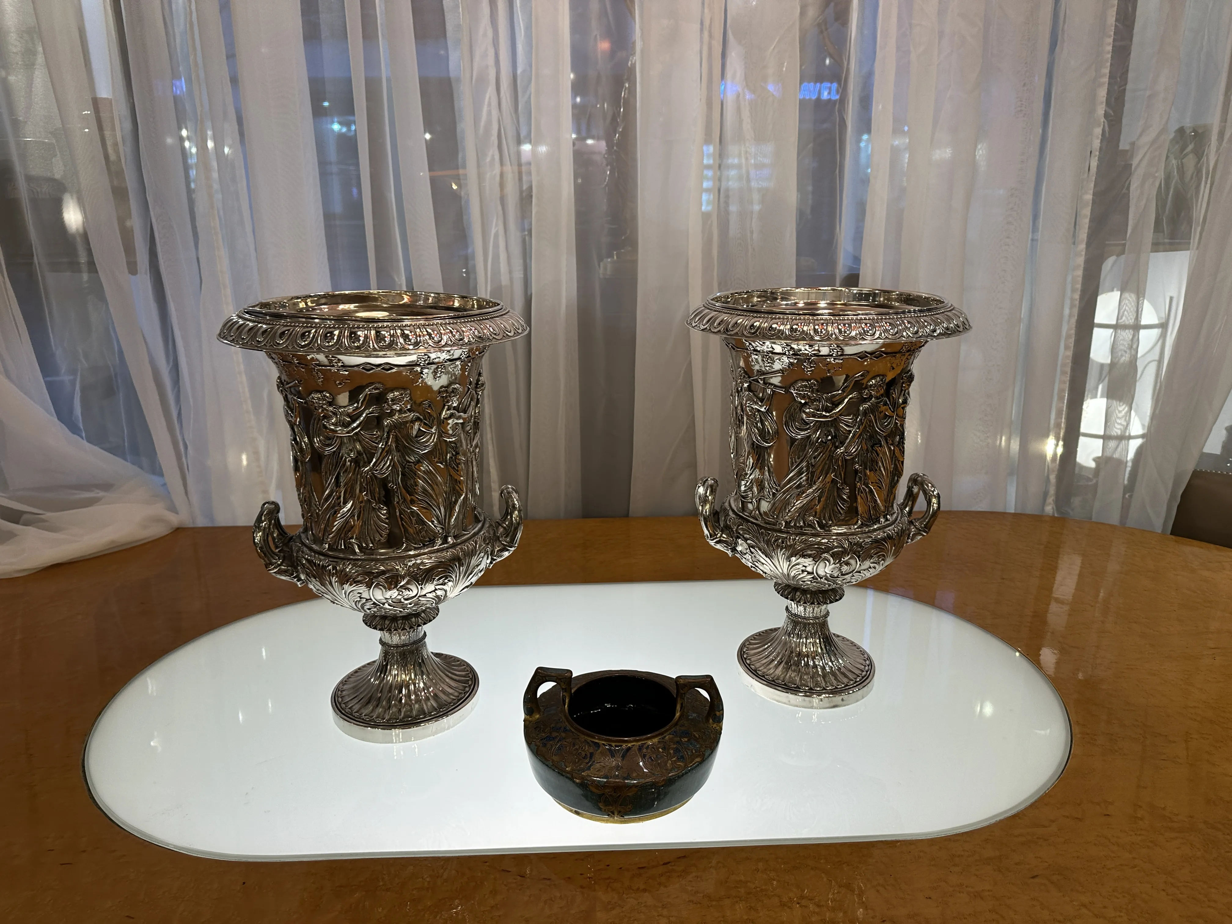 装飾的な古典陶器、浮き彫りの詳細と装飾が施され、滑らかなテーブルに展示されています。大きい作品が2つ、小さな作品が1つ。
