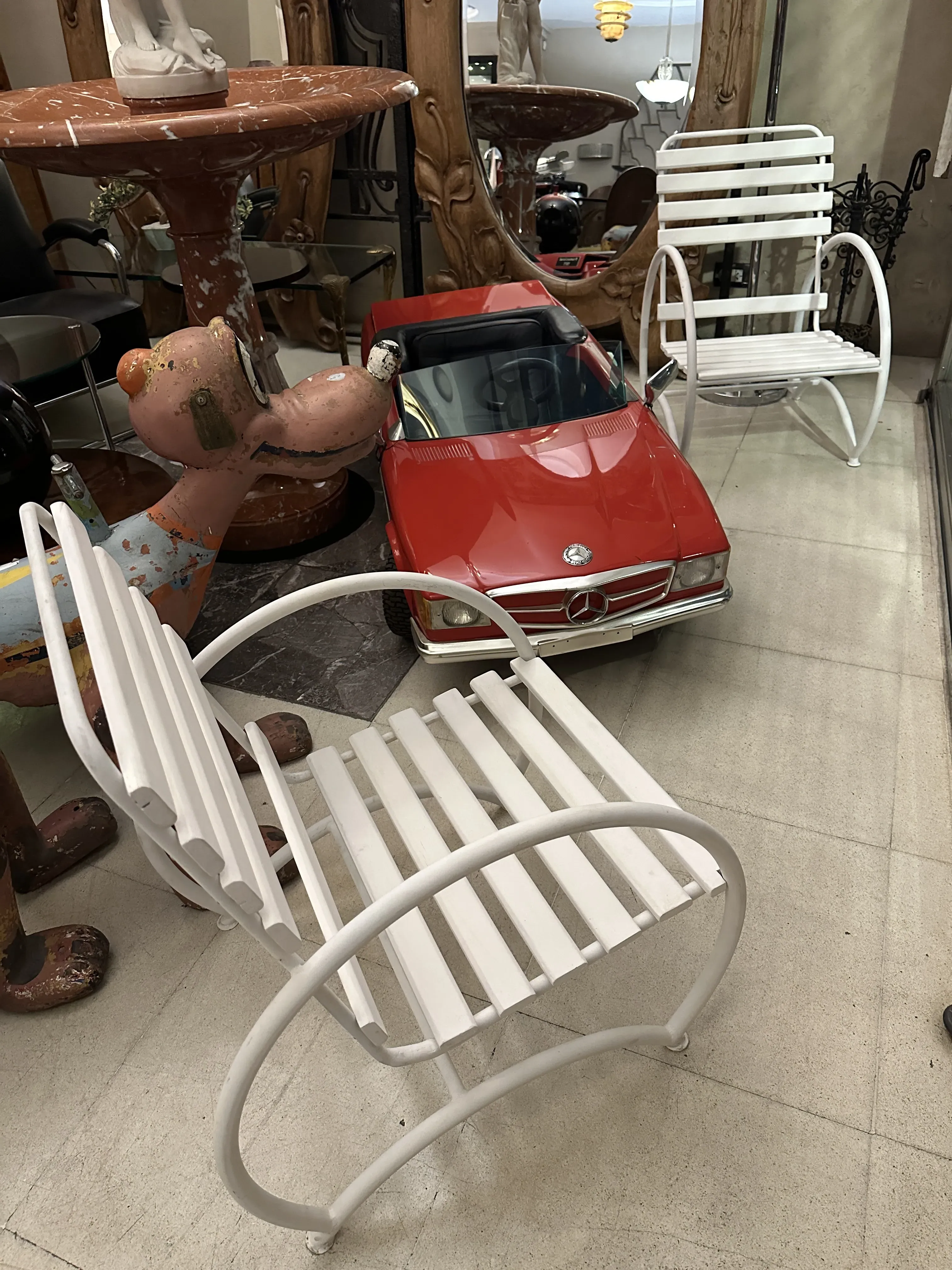 Two antique garden armchairs with classic design in a decorative setting with other items and a red car.
