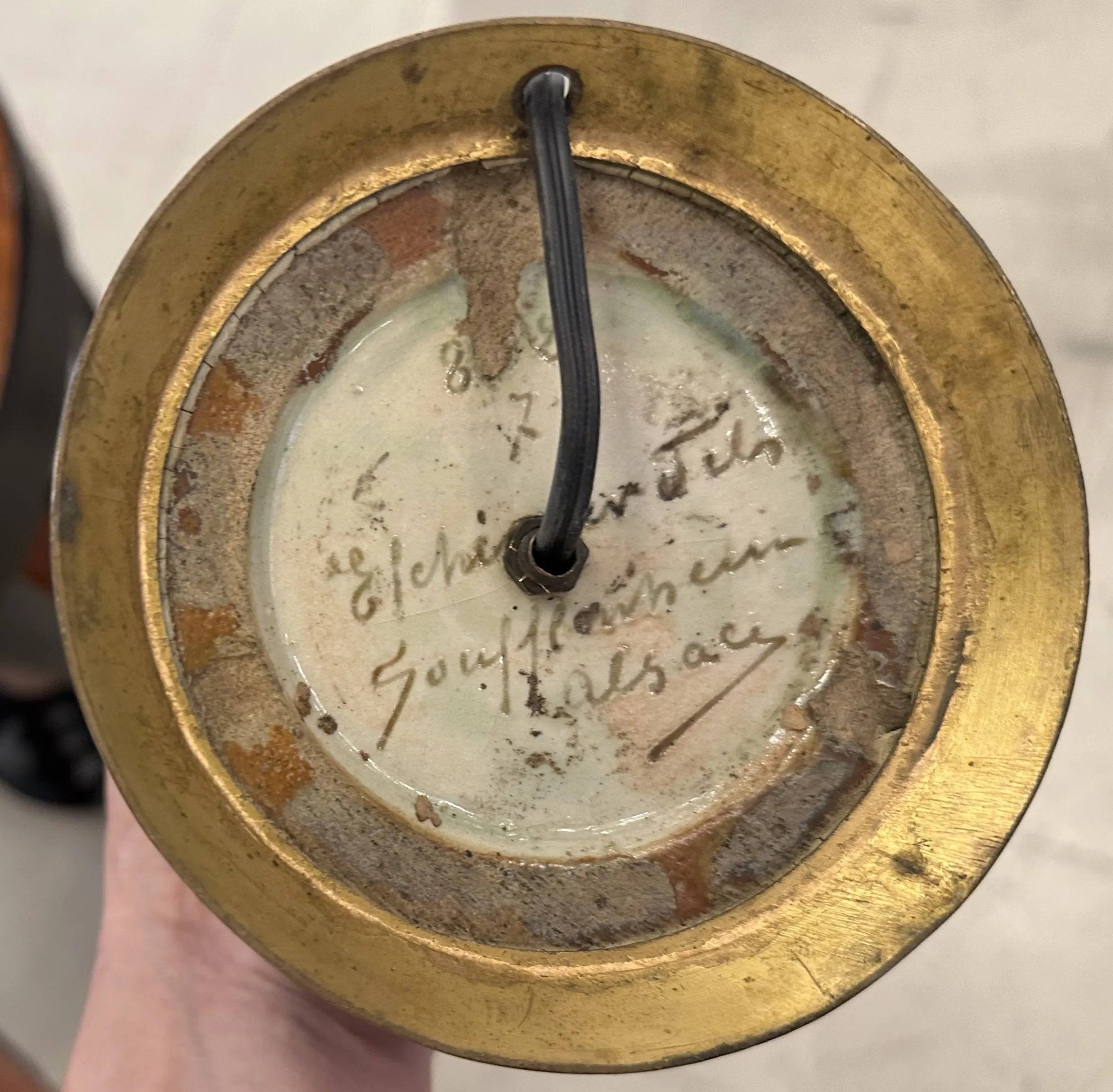 पुरानी टेबल लैंप के आधार का दृश्य जिसमें हस्ताक्षर हैं।