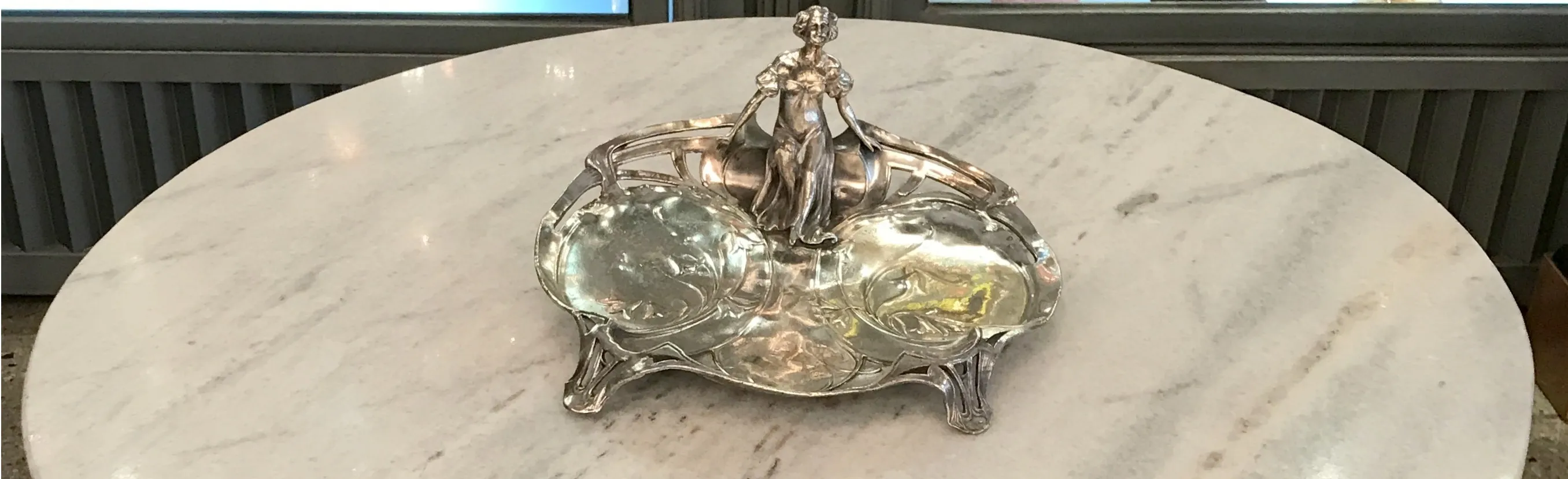 Elegante porta-cartões antigo com detalhes artísticos, decorado com uma figura feminina, sobre um fundo de mármore.