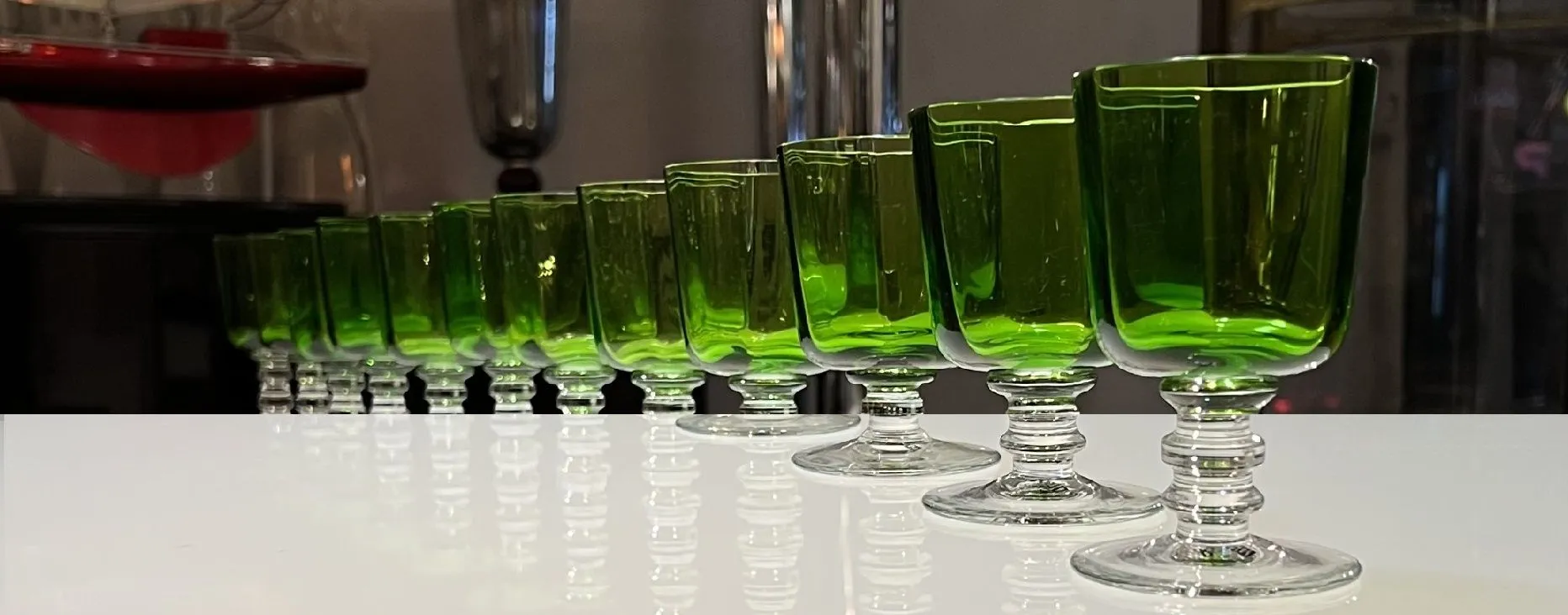 Antike grüne Gläser auf einem weißen Tisch aufgereiht, die feine Schatten werfen.