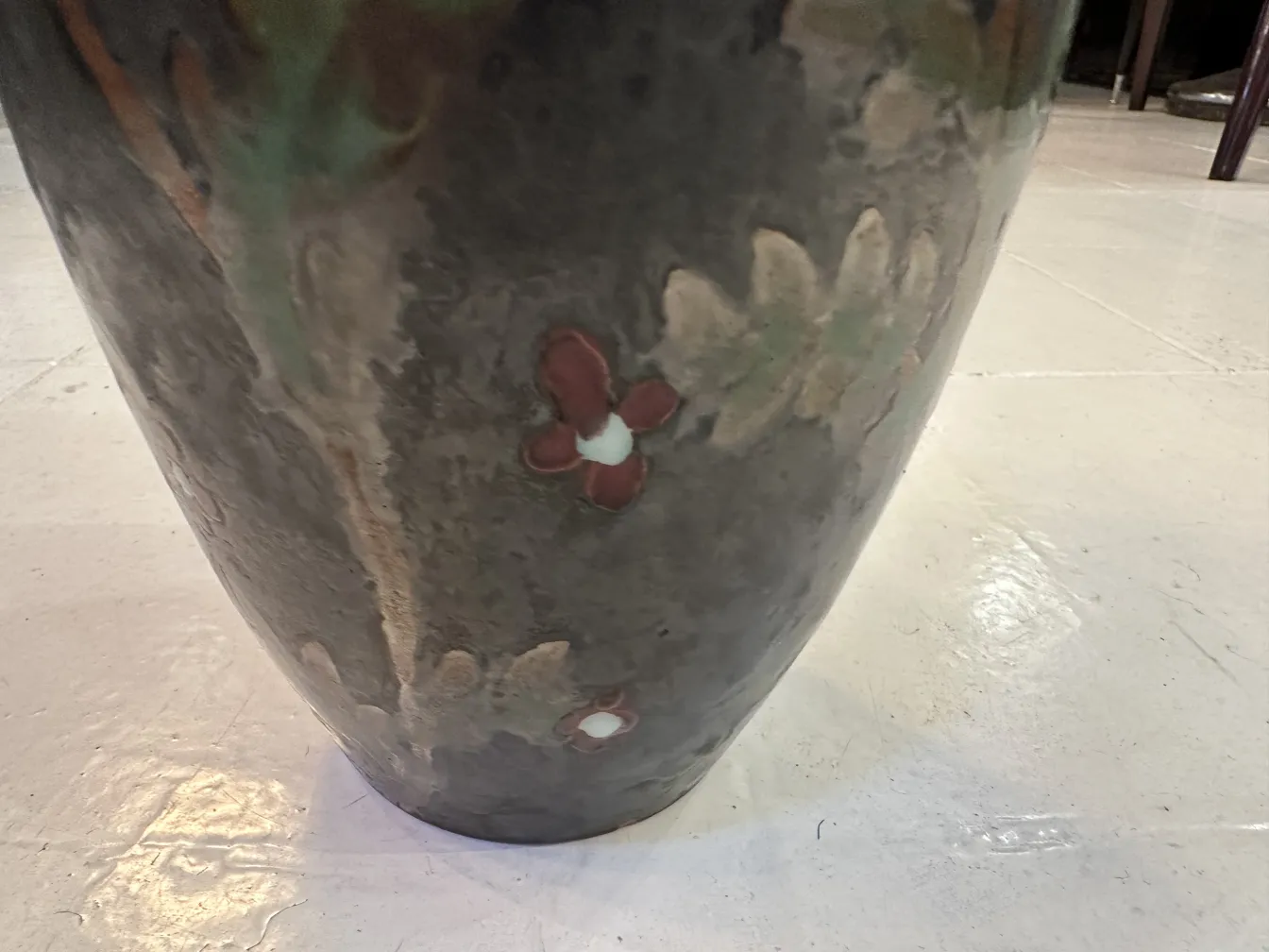 Vaso de cerâmica antiga decorado com flores coloridas em um ambiente simples.
