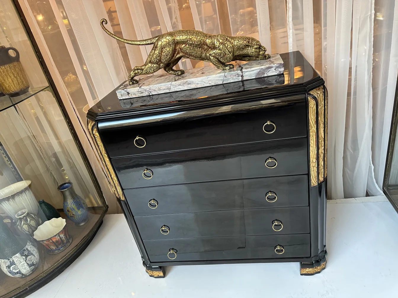 Cassettiera antica con finitura nera e dettagli dorati, decorata con scultura di felino.