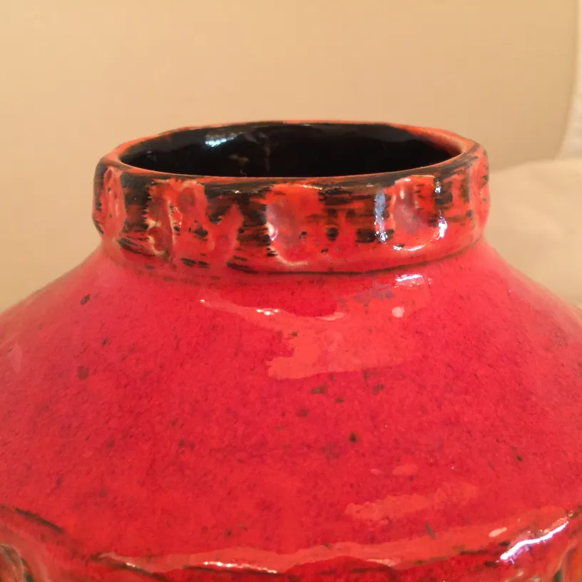 Antiga cerâmica vermelha brilhante com detalhes pretos e decorações sutis no topo.