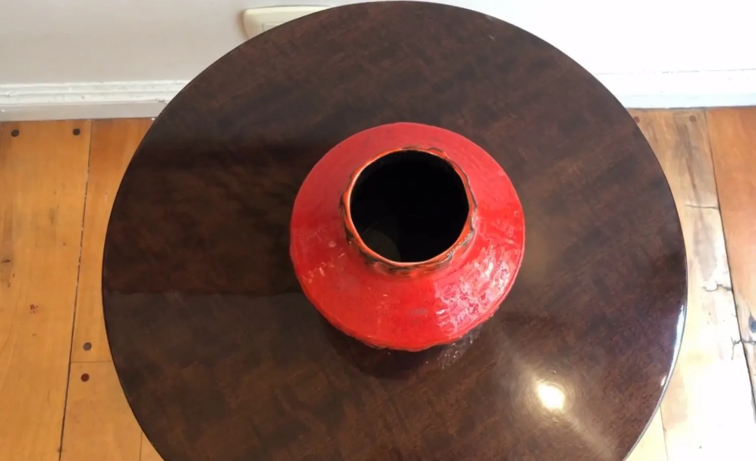 Antiga jarra de cerâmica vermelha com forma arredondada, em uma mesa de madeira.