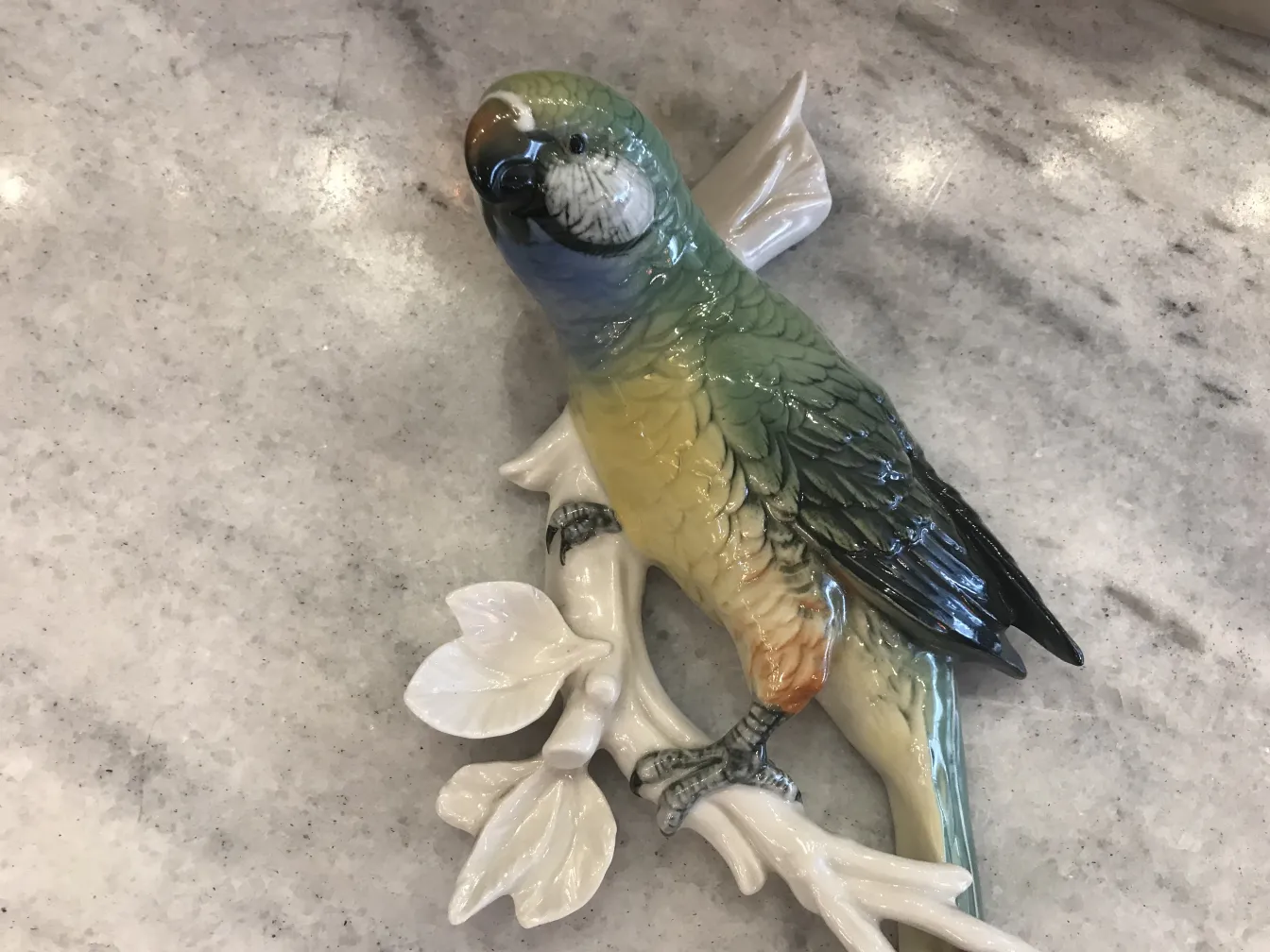 Figurine en céramique d'un perroquet sur une branche décorative.