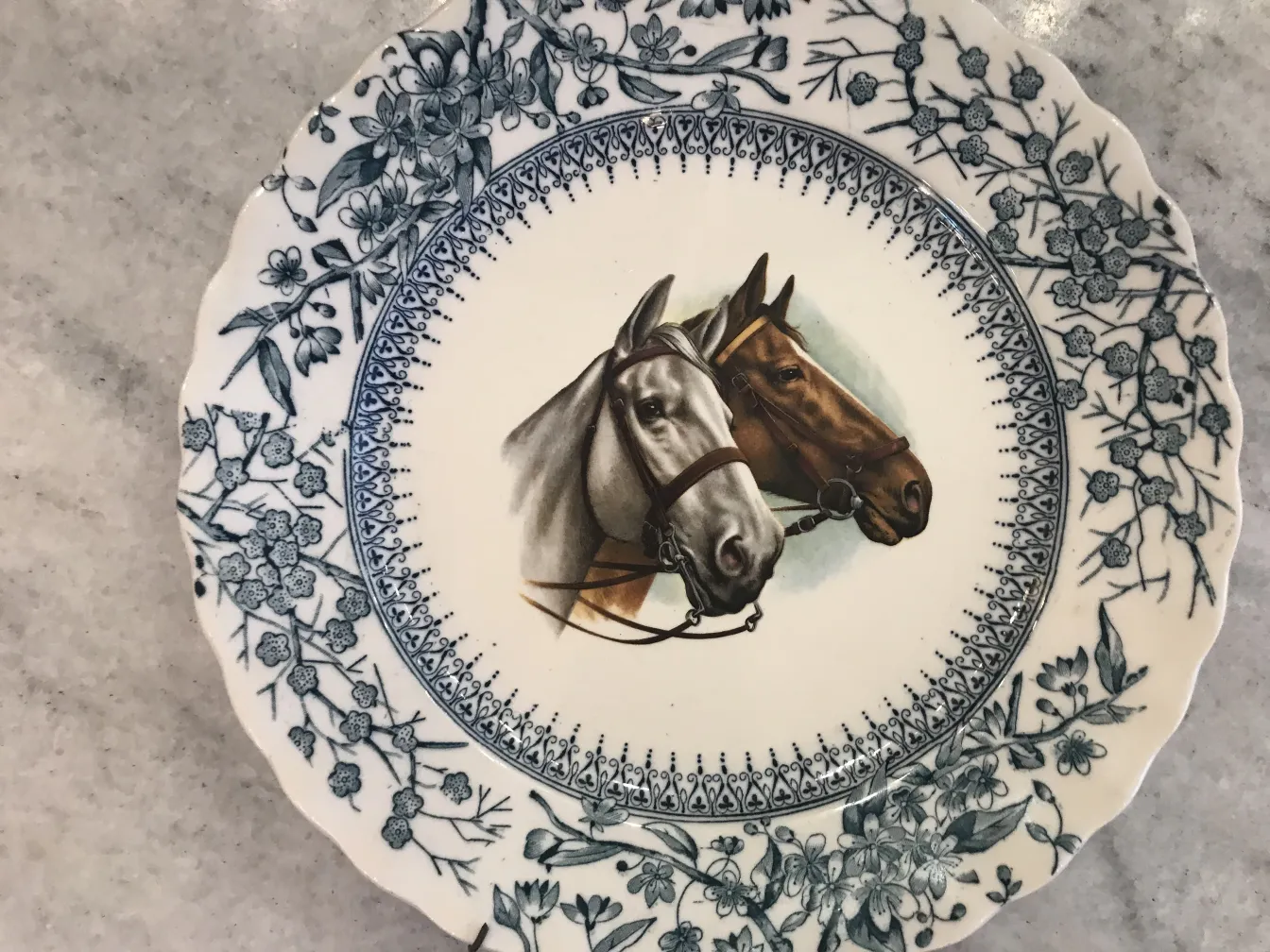 Plato antiguo de cerámica con imagen de caballos en Gloucester. Decoración floral alrededor.