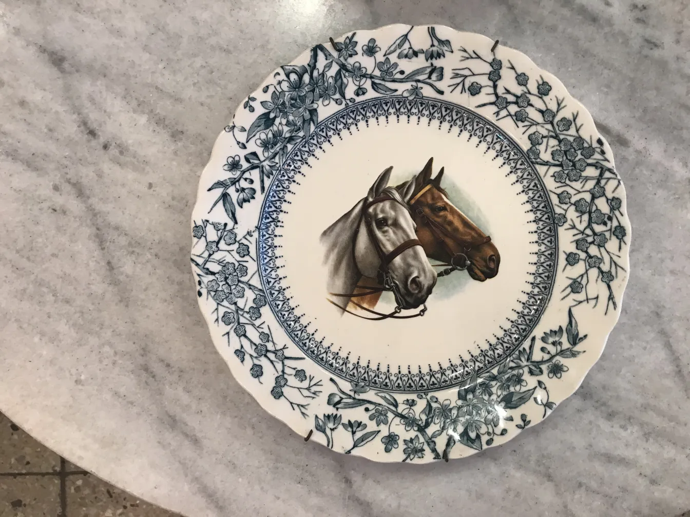 Antique ceramic plate featuring two horses, decorated in blue floral patterns.