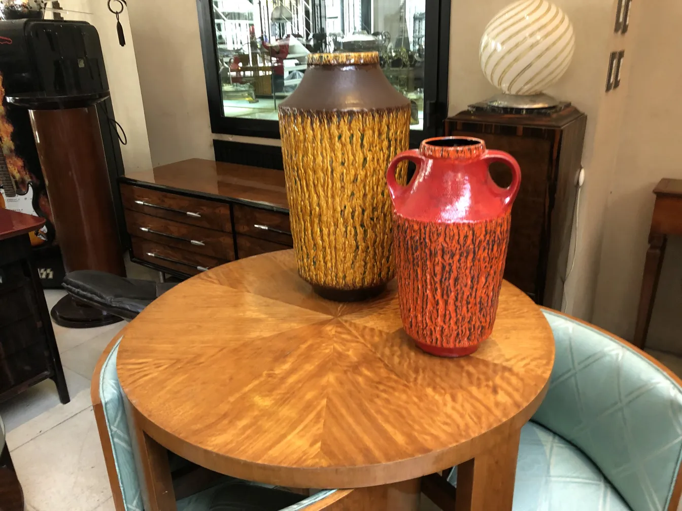 Dois vasos cerâmicos antigos coloridos sobre uma mesa. O vaso amarelo e o vermelho têm formas e decorações distintas.