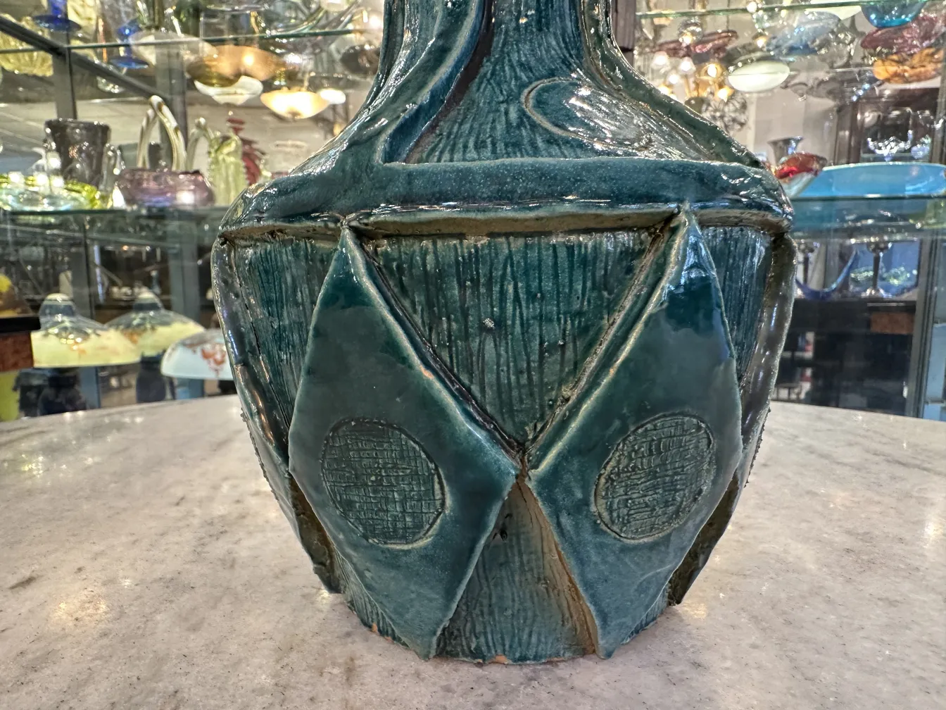 浮彫りデザインと光沢仕上げの古代陶器の花瓶が、アンティークに囲まれています。