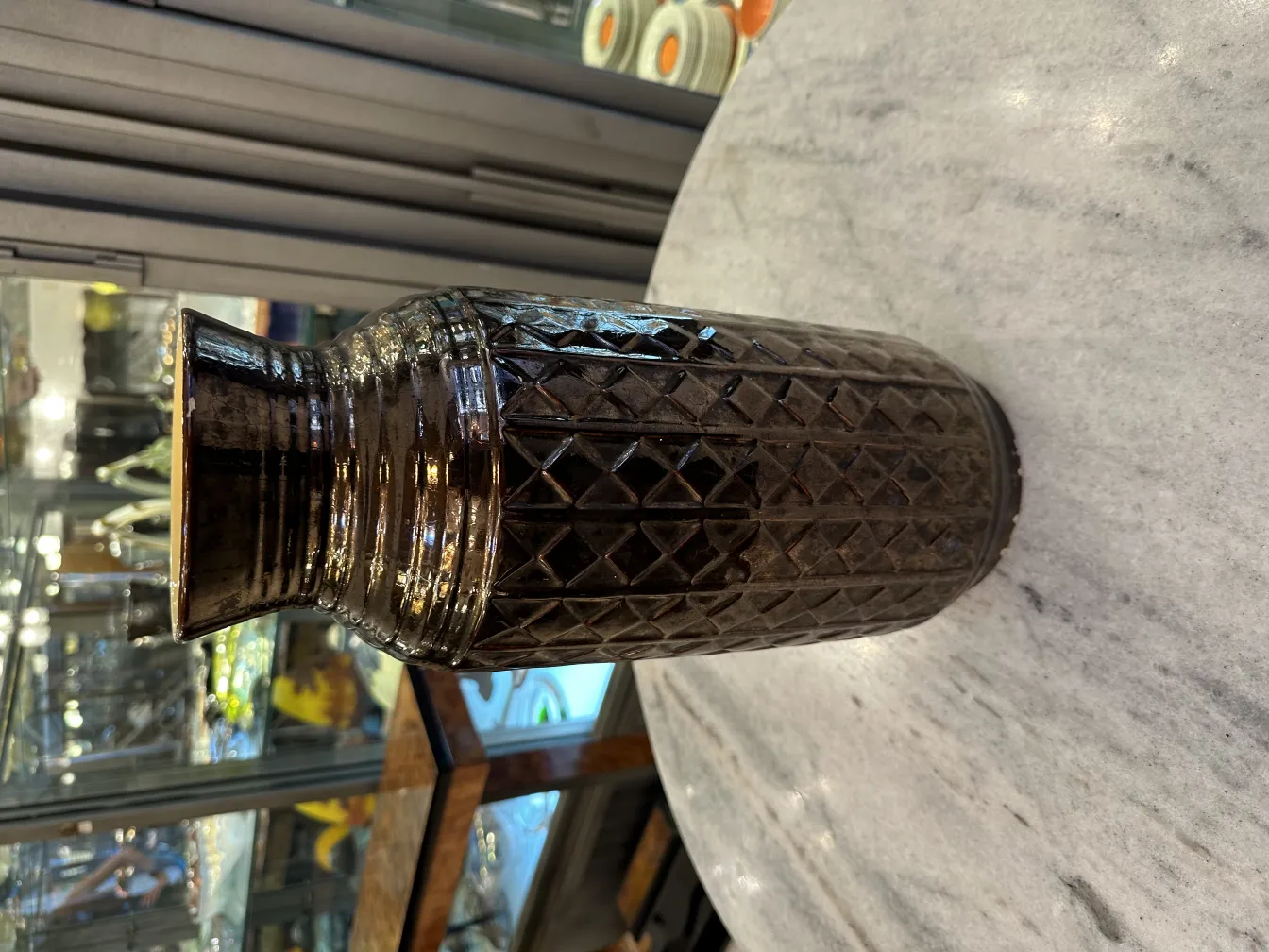 Jarra antiga de cerâmica com padrão de diamante, superfície brilhante em um ambiente elegante.