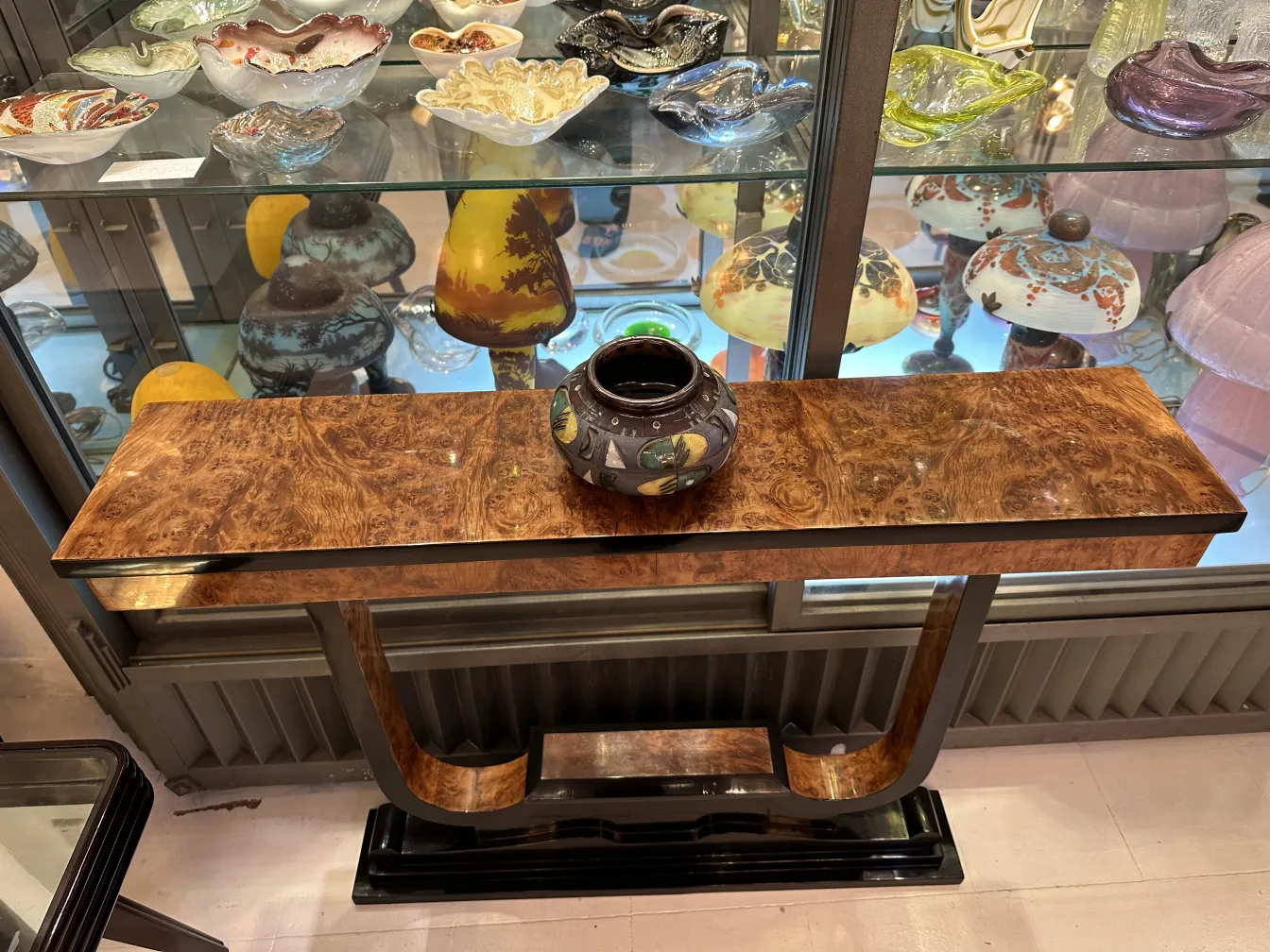 Antiga cerâmica decorativa sobre uma mesa de madeira com vários objetos ao fundo.