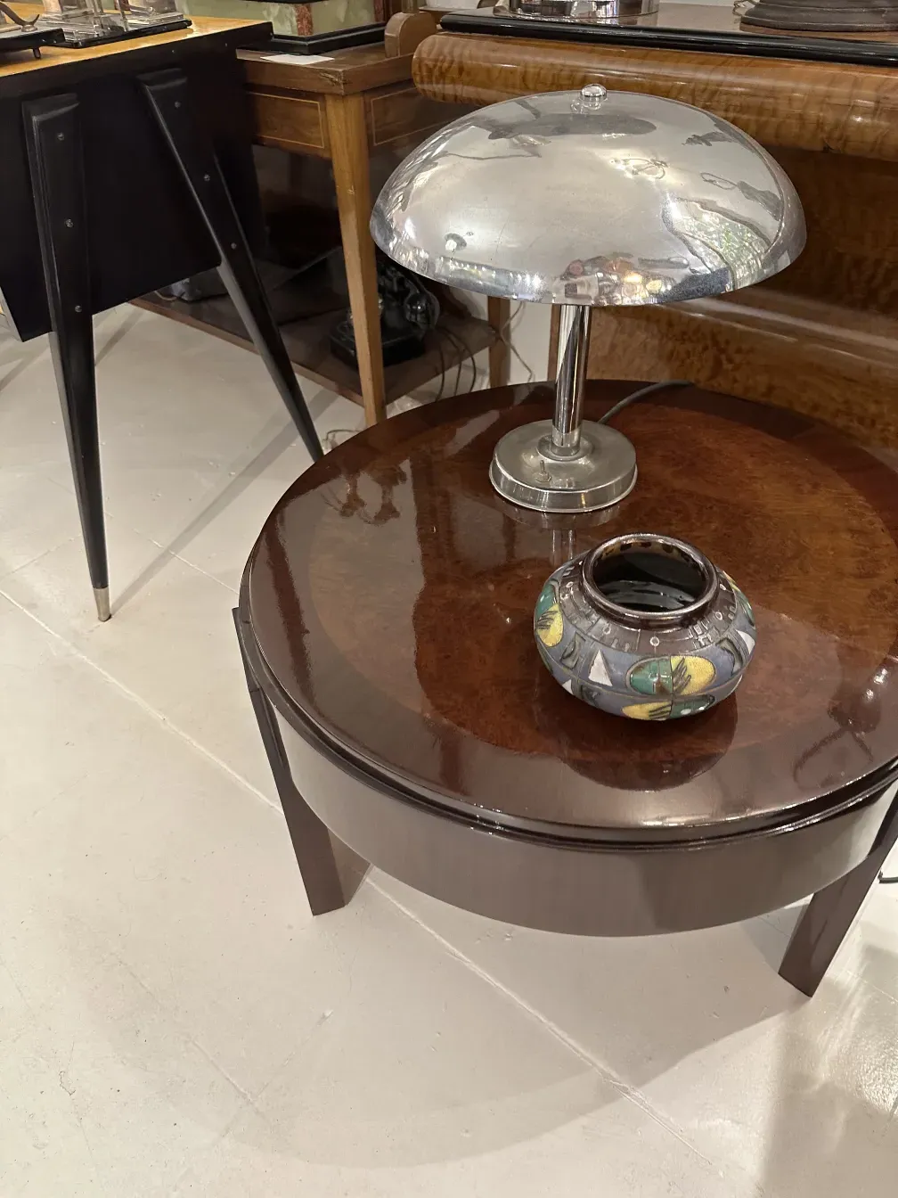 Peça de cerâmica antiga com cores vibrantes em um ambiente elegante com lâmpada e mesa.