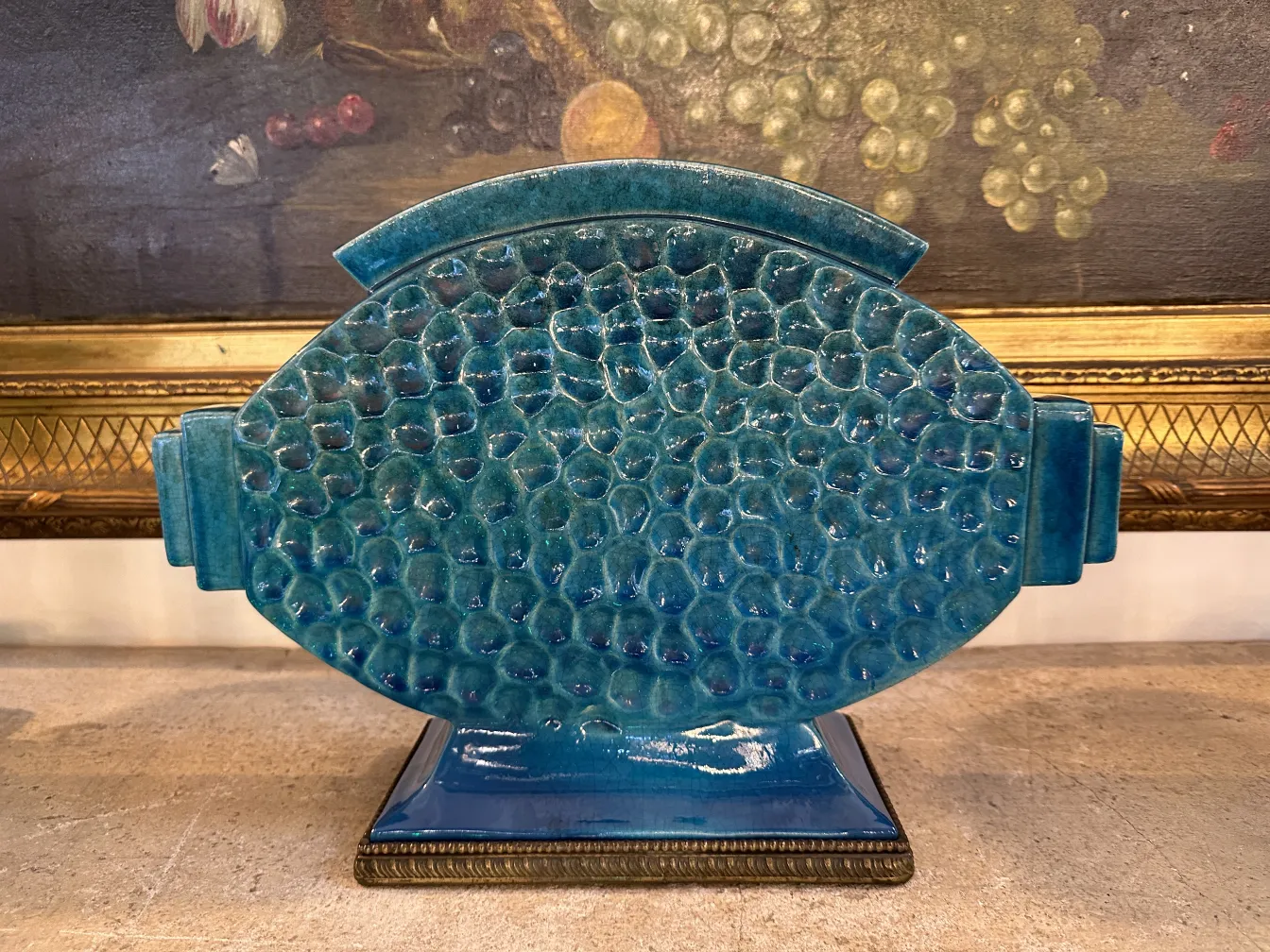 Cerámica antigua de color azul con textura y forma ovalada, decorada, en un ambiente clásico.