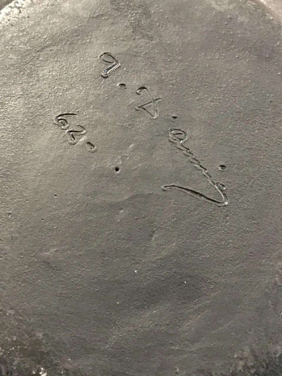 Base di ceramica antica con firma distintiva, tonalità scura.