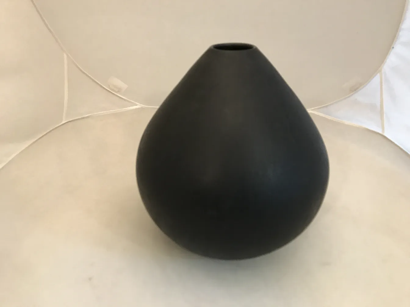 Antique black ceramic in teardrop shape against a light background.