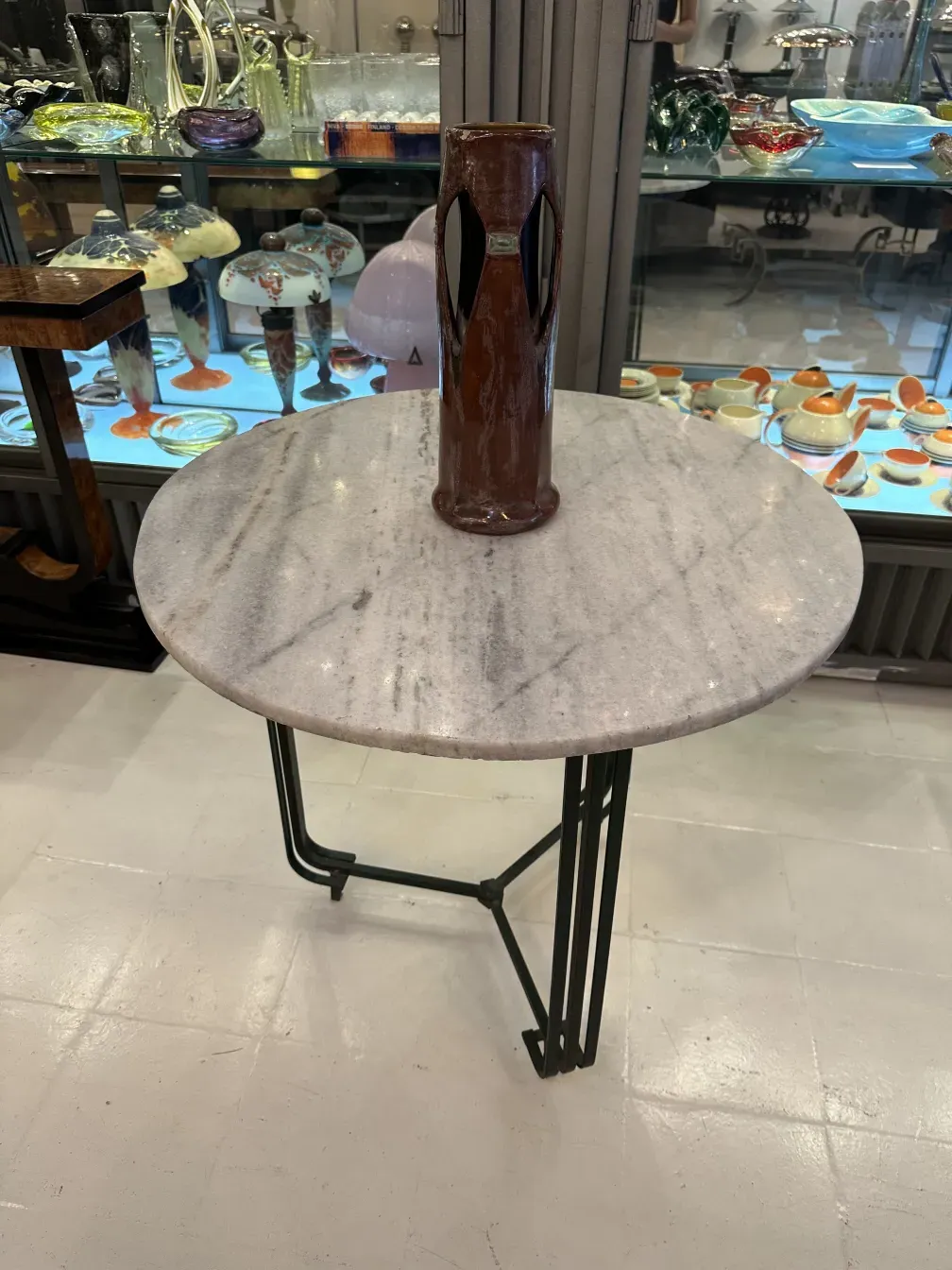 Vaso cerâmico marrom sobre mesa redonda em ambiente antigo.