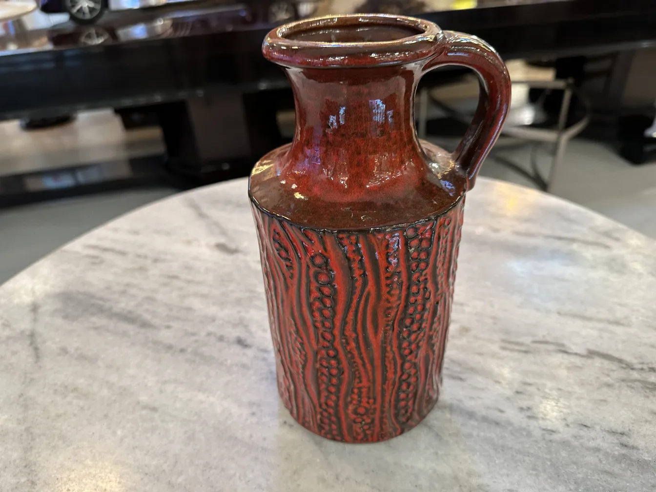 Vaso antico in ceramica artigianale con decorazioni in rilievo e colore rosso, posato su un tavolo di marmo.
