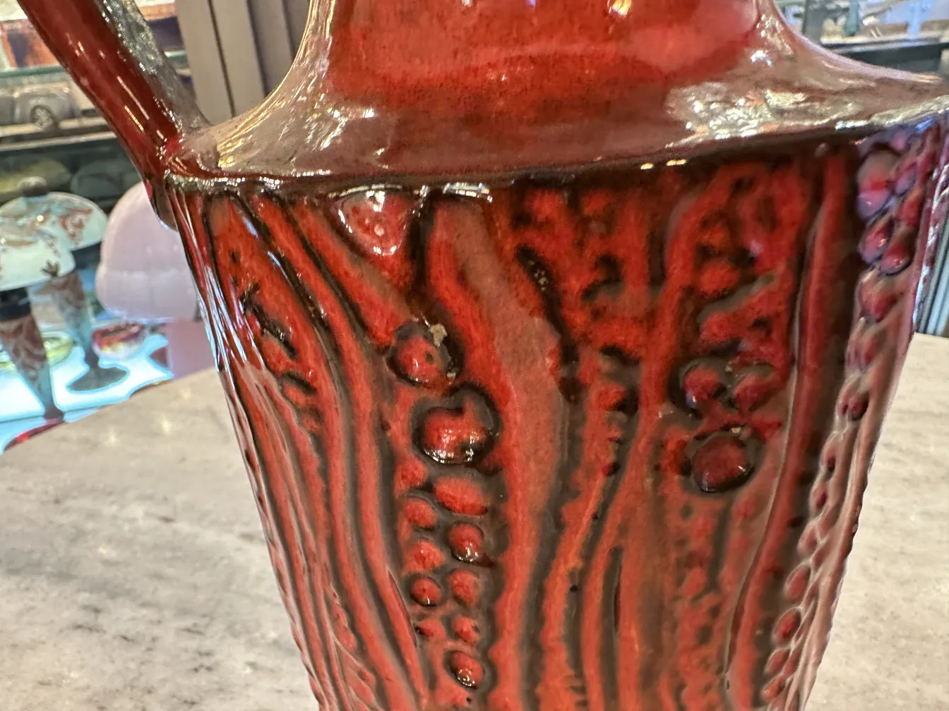 Antique ceramic jug with red and black textured surface.