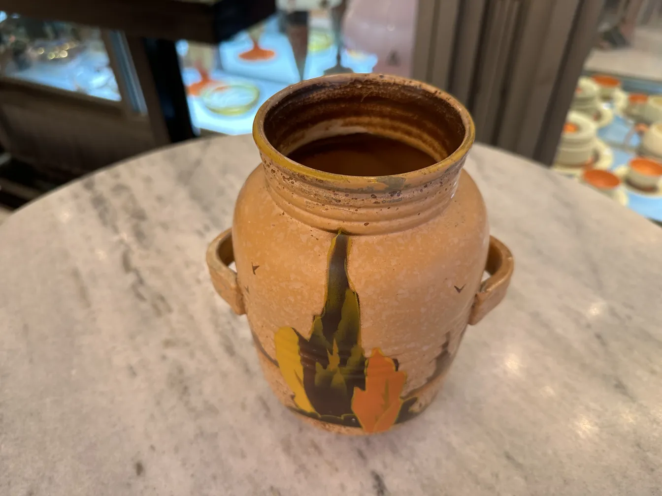 Vaso in ceramica antica con design naturale in tonalità Terre, posato su un tavolo con sfondo sfocato.