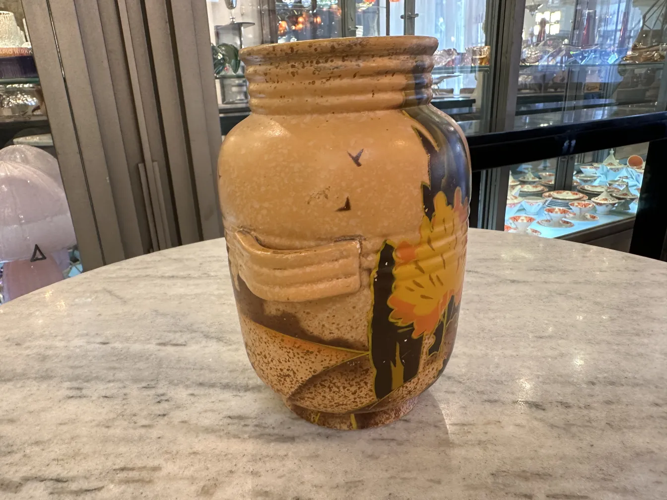 Vaso de cerâmica antiga com decoração floral vibrante em tons quentes sobre fundo claro.