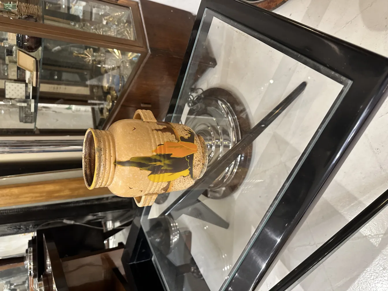 Vase ancien en céramique décoré de motifs de feuilles et de couleurs chaudes, dans un environnement élégant.