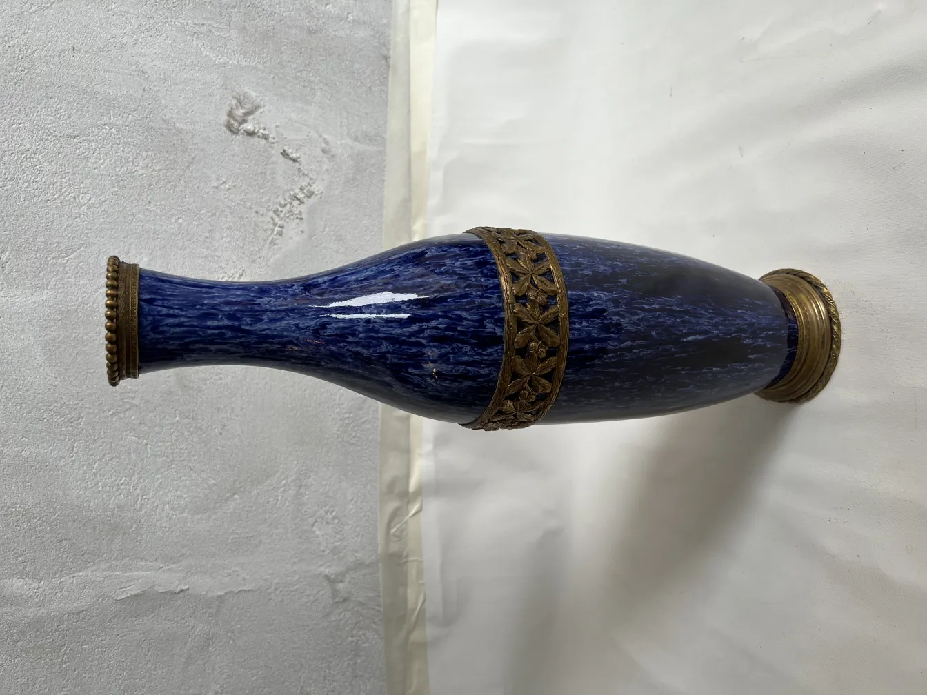 Antique ceramic vase in blue tones with golden embellishments against a neutral background.