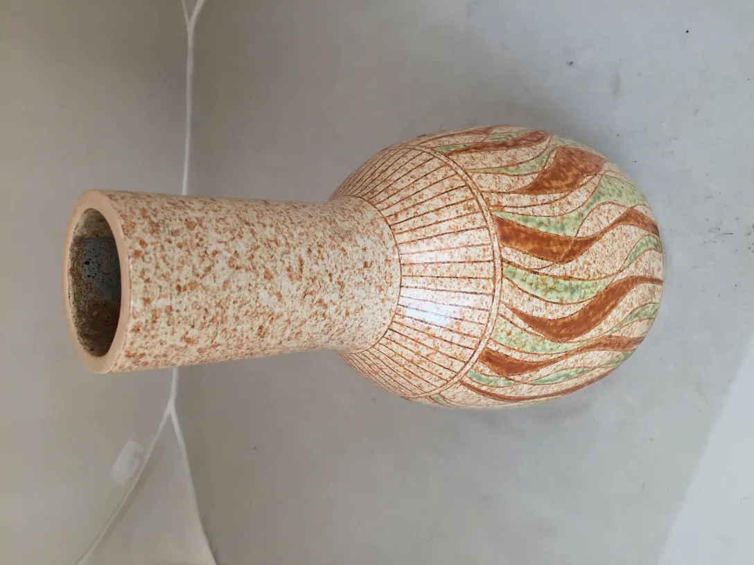 Vasija antigua de cerámica decorada con motivos en tonos terracota y verde, fondo claro.