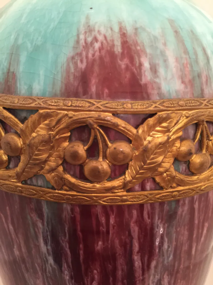 Vaso de cerâmica antiga com matizes verdes e vermelhos, adornado com detalhes dourados de folhas e frutos.