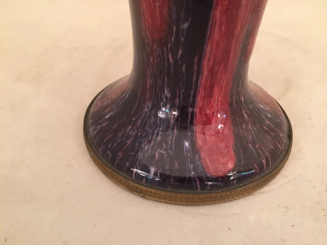 Vaso de cerâmica antiga com design vermelho e preto, colocado em um ambiente neutro.