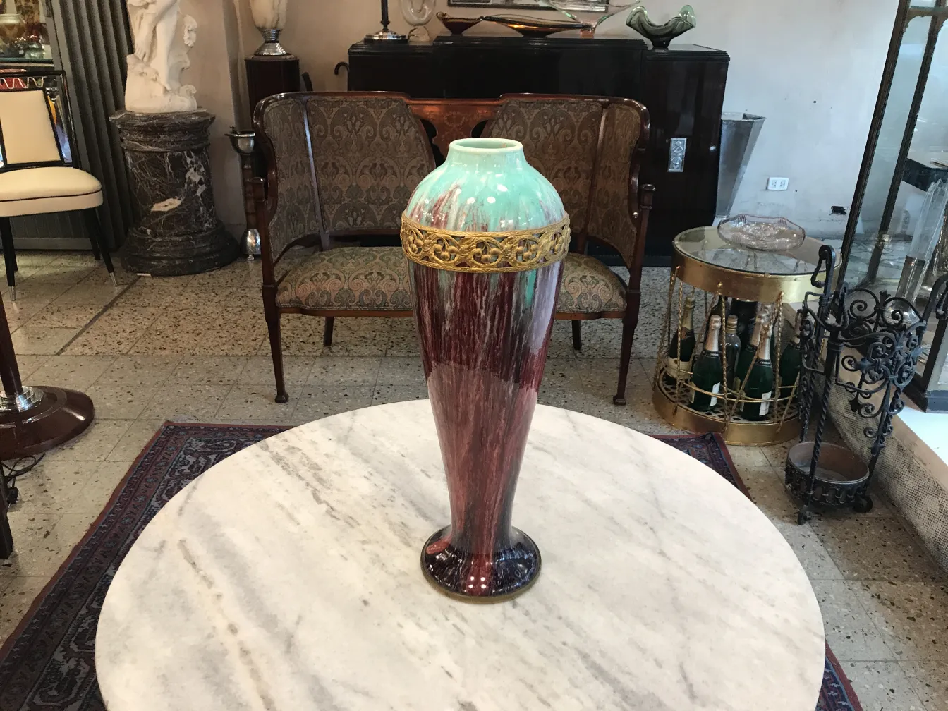 Vase ancien en céramique avec des détails dorés et des tons verts et rouges, placé sur une table en marbre.